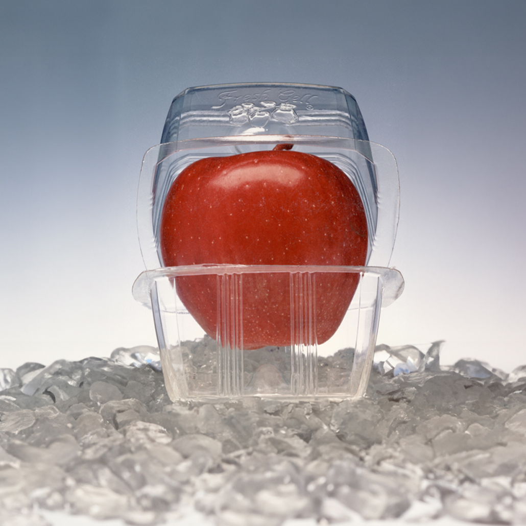 Red apple securely placed in a transparent plastic container surrounded by ice, highlighting the protective packaging designed to preserve the fruit's freshness.